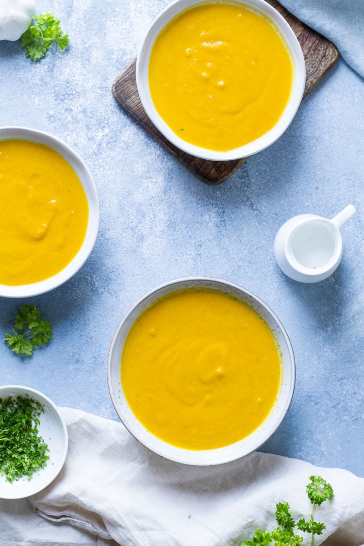 Three bowl with carrot soup on blue table. Flatlay.