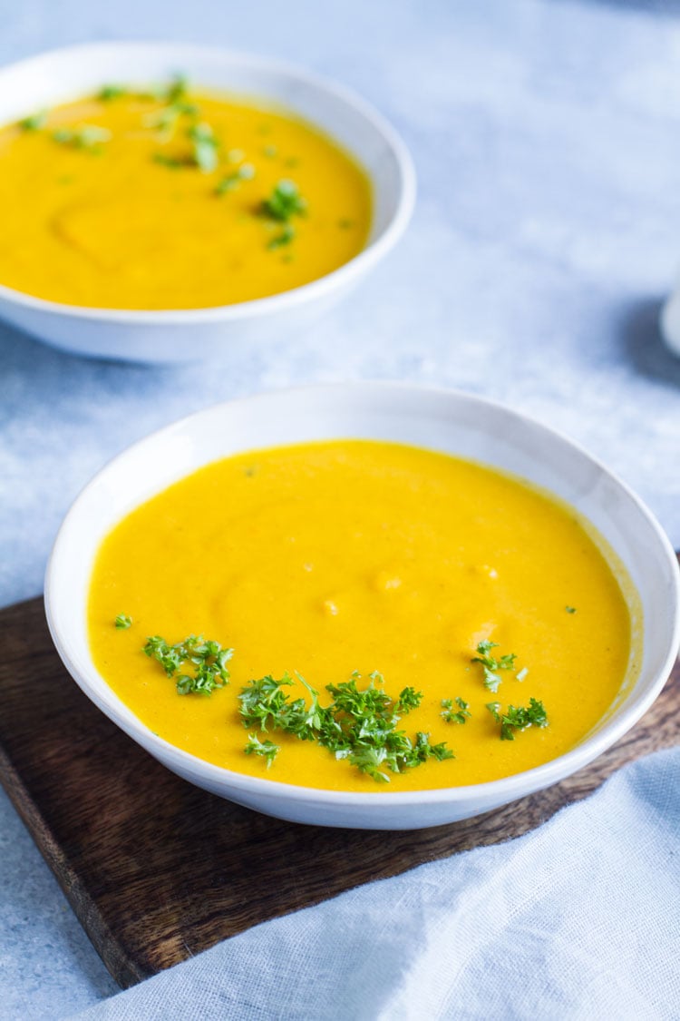 Two bowl of carrot soup with fresh parsley garnish.
