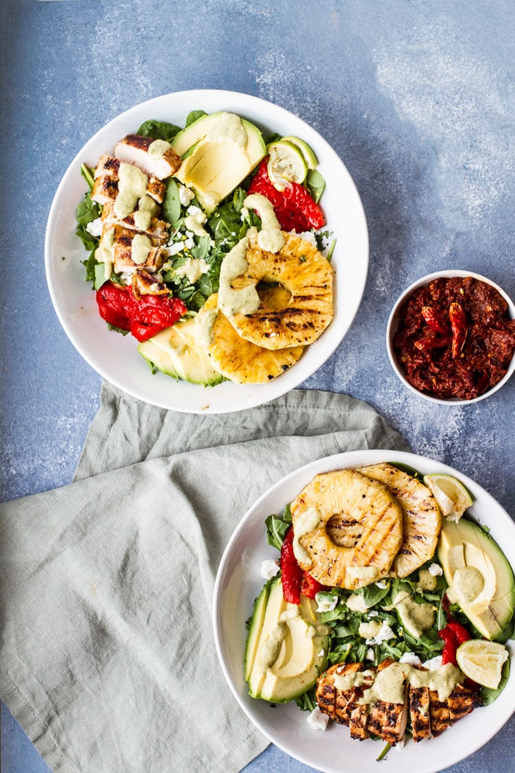 Two large white bowls with grilled harissa chicken salad, harissa paste in a smaller bowl.