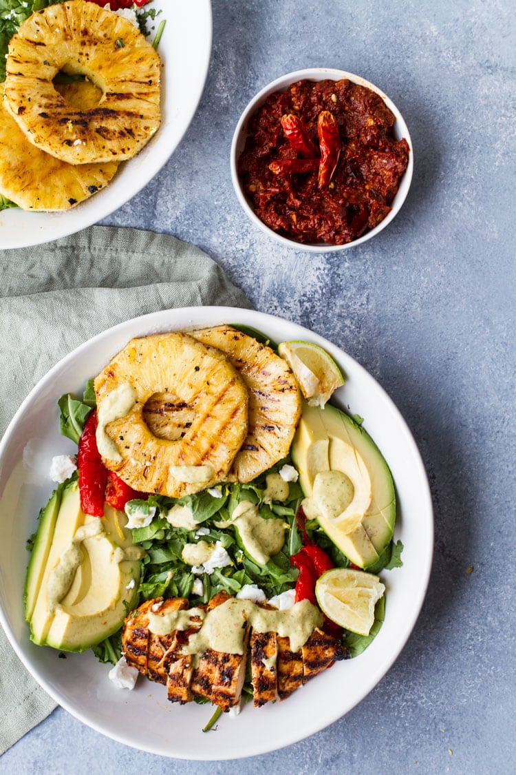Big white bowl with whole chicken breast, slices of grilled pineapple, avocado slices and more.
