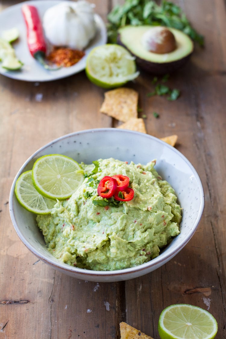 Guacamole in a bowl and ingredients for this easy guacamole recipe in the background.