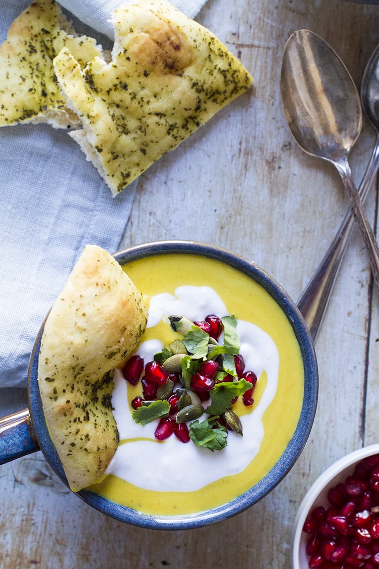 Butternut squash soup with ginger cream, pomegranates, pepitas and naan. Flat lay.