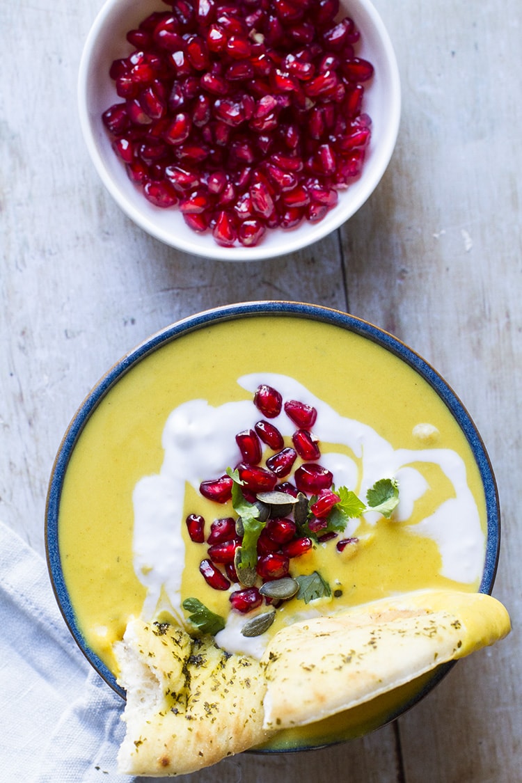 Yello soup with coconut cream and pomegranate arils. Naan on the side. Flat lay.