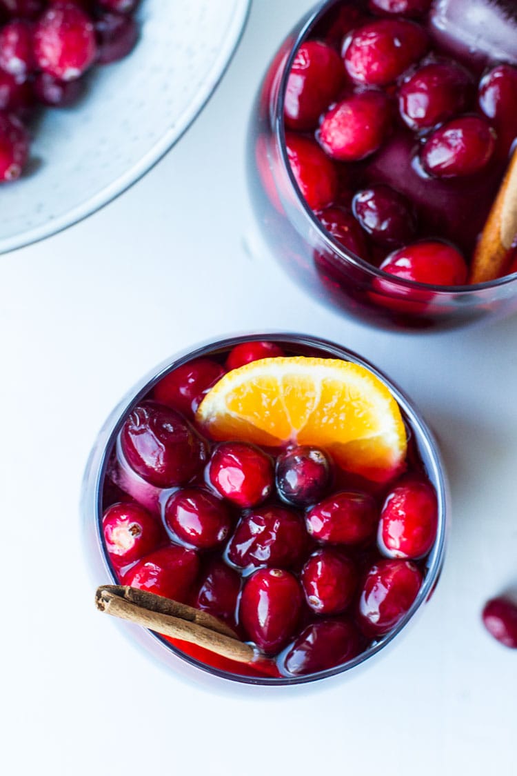 Two glasses with fresh cranberries, cinnamon stick and orange slice.