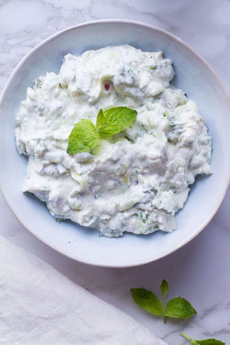 Raita yoghurt sauce in a blue bowl, garnished with mint. Flatlay.