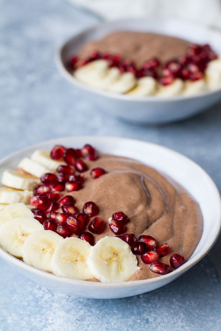 Pudding in a blue bowl, topped with banana and pomegranate.