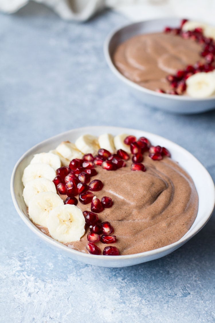 One blue bowl with chocolate chia pudding, decorated with banana slices and pomegranate seeds on one side.
