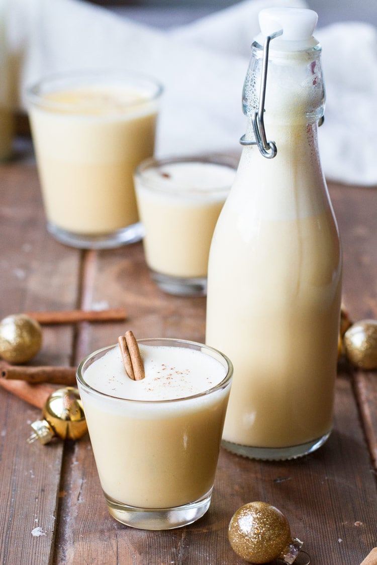 Glass and bottle with eggnog. Gold ornaments around on a wooden table.