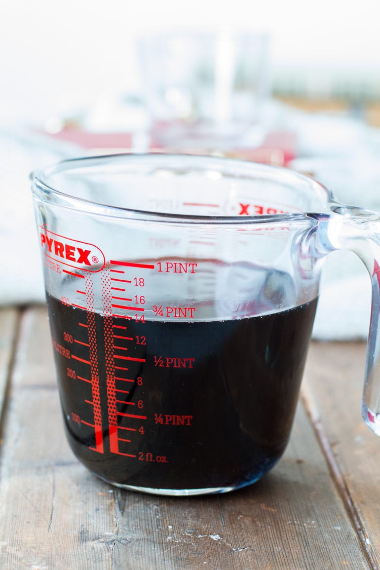 Blackcurrant syrup in a measuring cup.