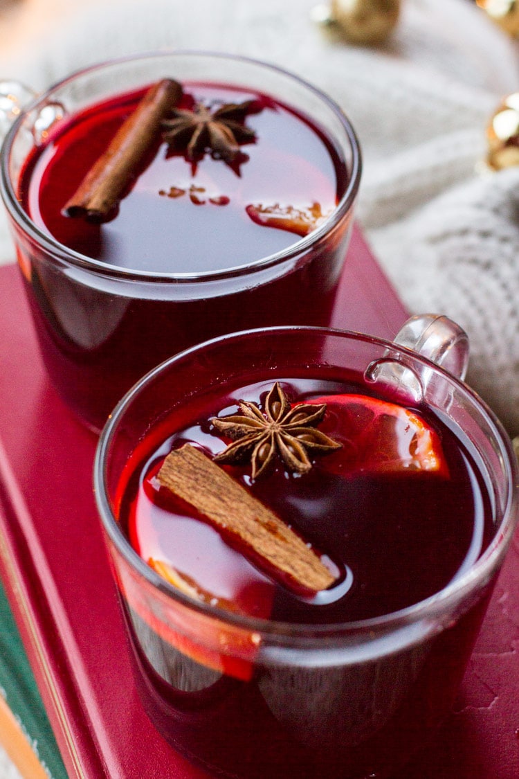 Two mugs with mulled wine garnished with cinnamon stick, star anise and clementine slice.