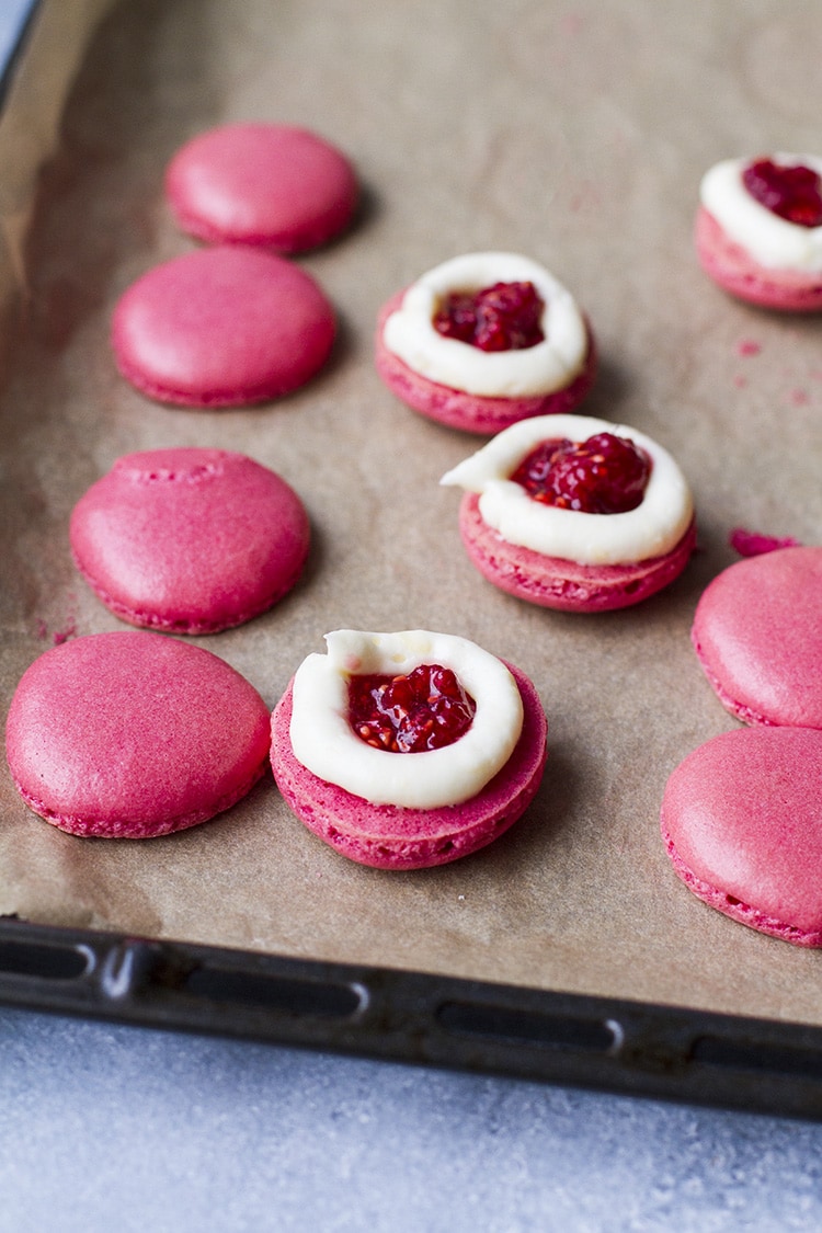 Open pink macaron with raspberry filling with white chocolate around it.