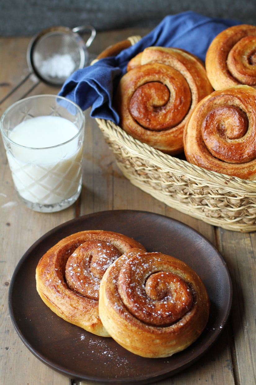 Cinnamon rolls on a wooden plate. More in the background.