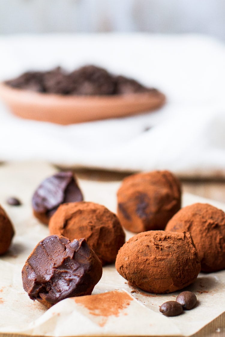 Chocolate Coffee Truffles on brown parchment paper. One is taken a bite of. Covered in cocoa powdered. A plate of coffee beans in the background.