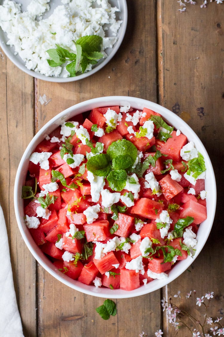 Watermelon salad in a white bowl on a wooden table, flatlay.