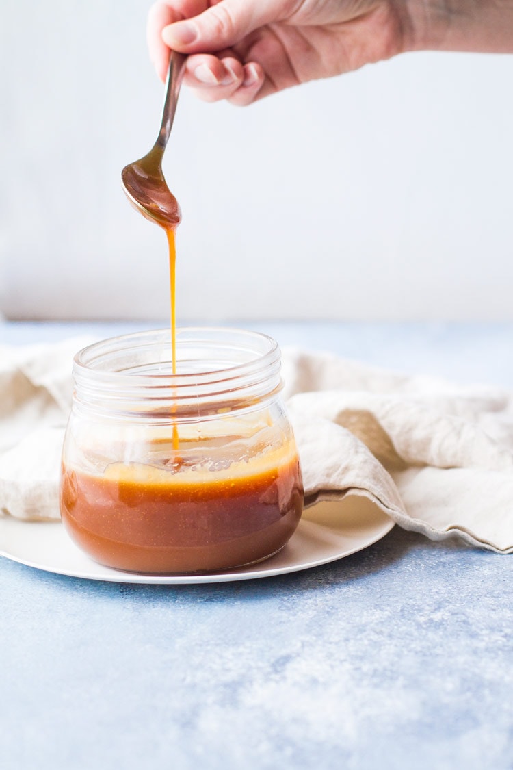 Glass jar with salted caramel sauce, hand with spoon drizzling into the jar.