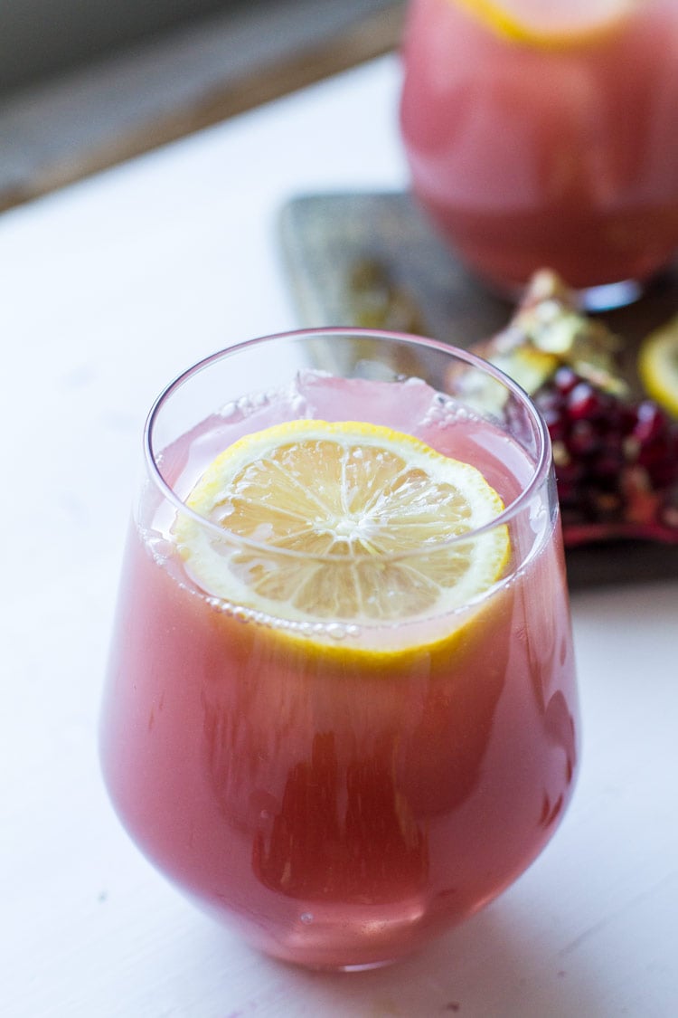 Stemless wine glass with pomegranate vodka lemonade and lemon garnish, closeup.