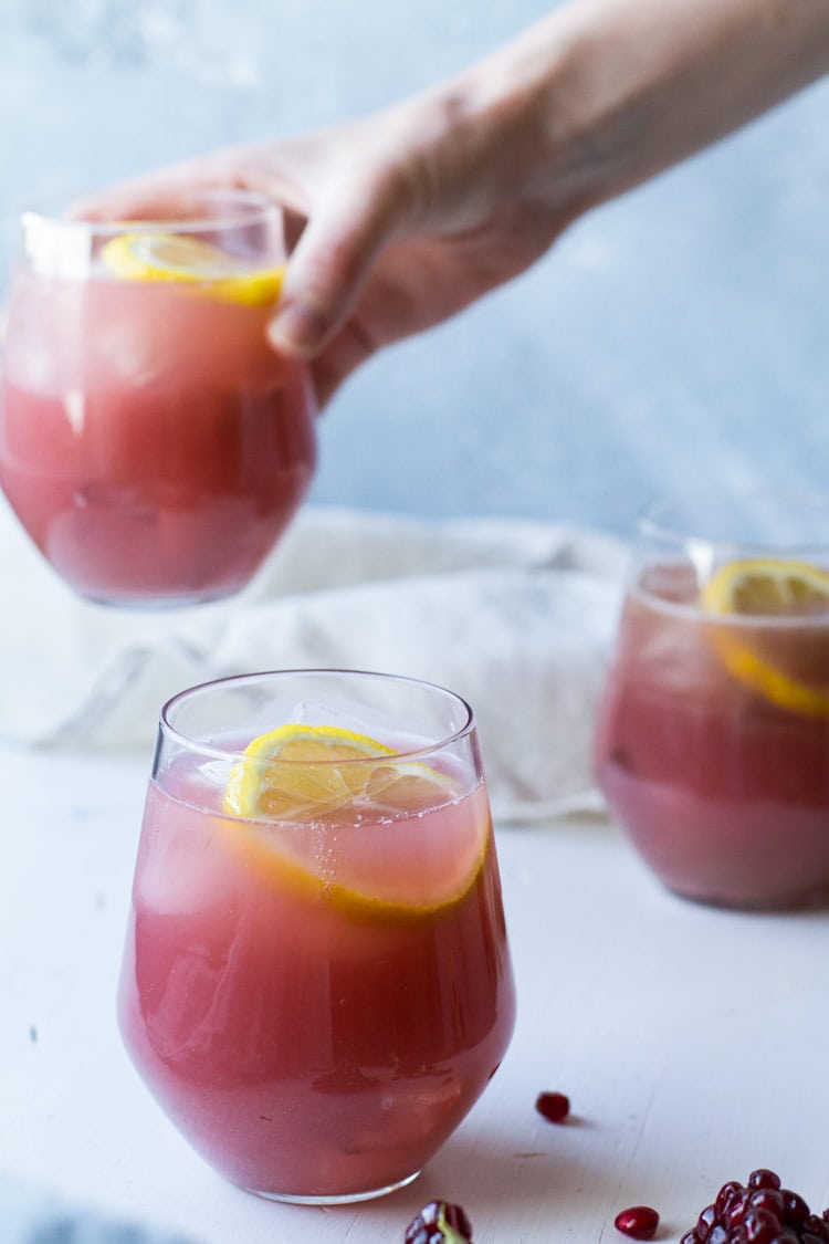 Three glasses with pink pomegranate lemonade, hand taking one of them.