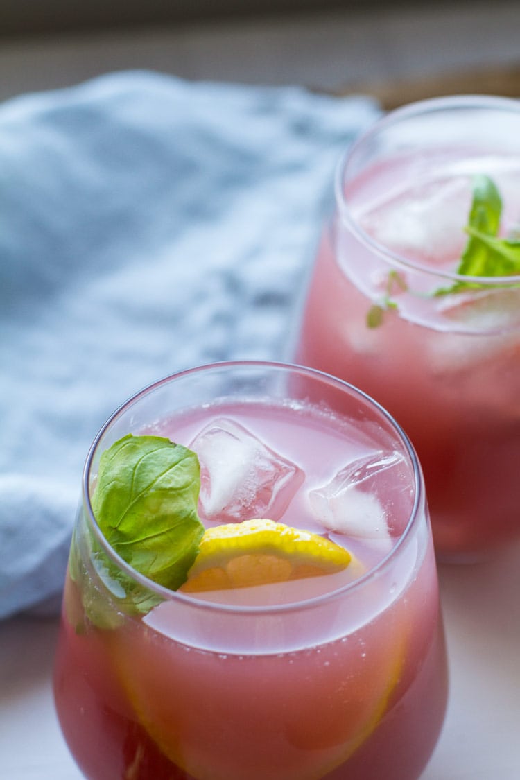 Two glasses with pink lemonade, garnished with ice cubes and mint sprig.