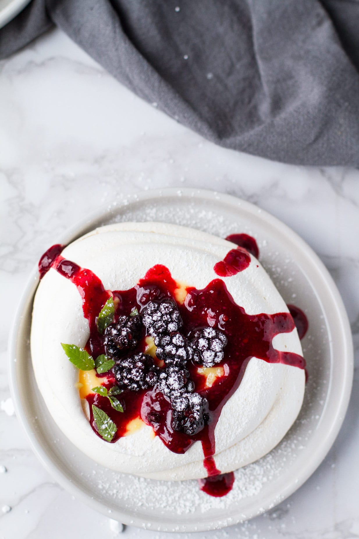 One pavlova nest with fresh blackberries and blackberry syrup running down the sides. Flatlay.