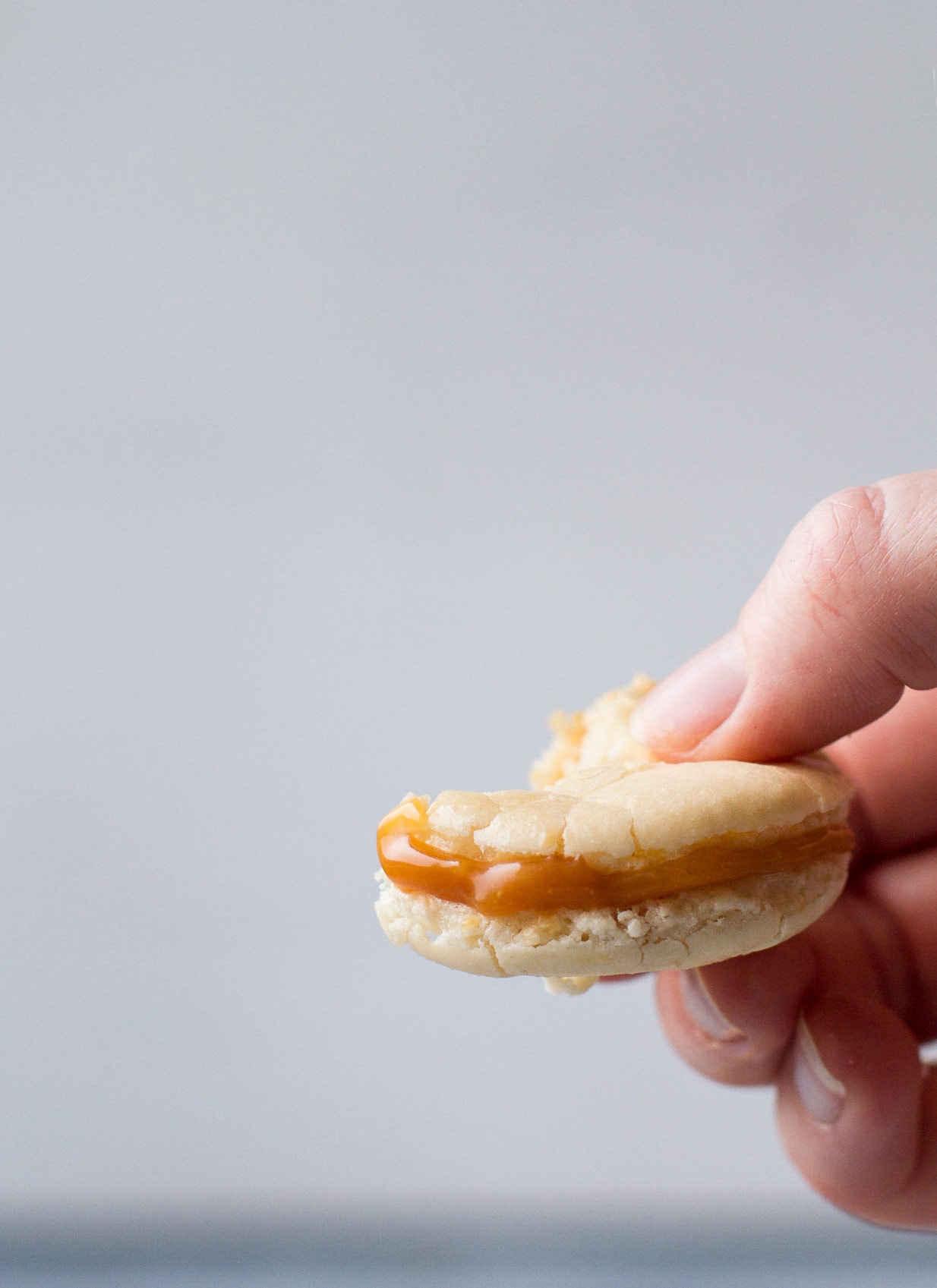 hand holding a salted caramel macaron taken a bite out of.