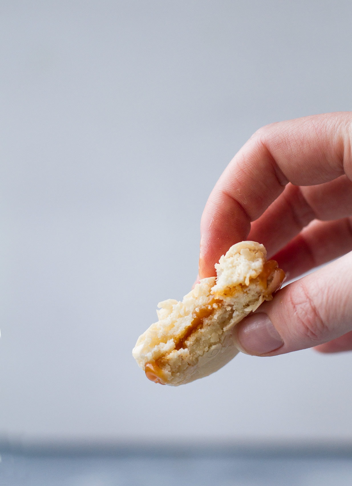 hand holding a salted caramel macaron that is taken a bite out off, off white background.