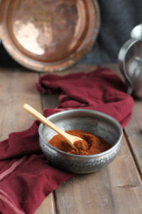 Baharat spices in a metal bowl and wooden spoon. Copper and wooden background.