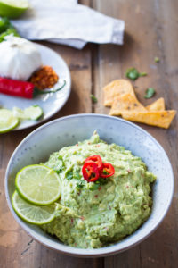 Chunky spicy guacamole in a bowl with three chilli slices and two lime slices.