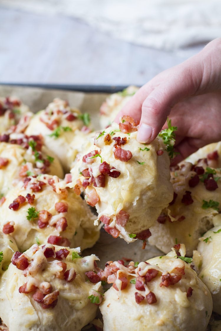Grabbing one homemade dinner rolls with cheese and bacon.