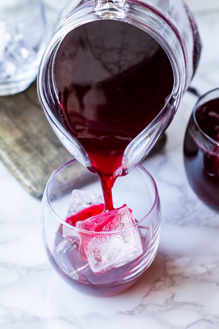 Pouring hibiscus tea into a glass with ice.