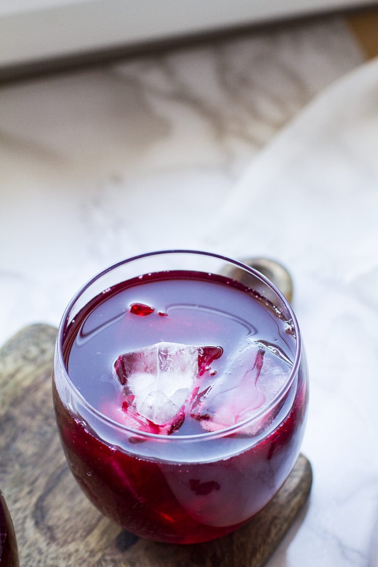 A round glass with hibiscus tea and ice cubes.