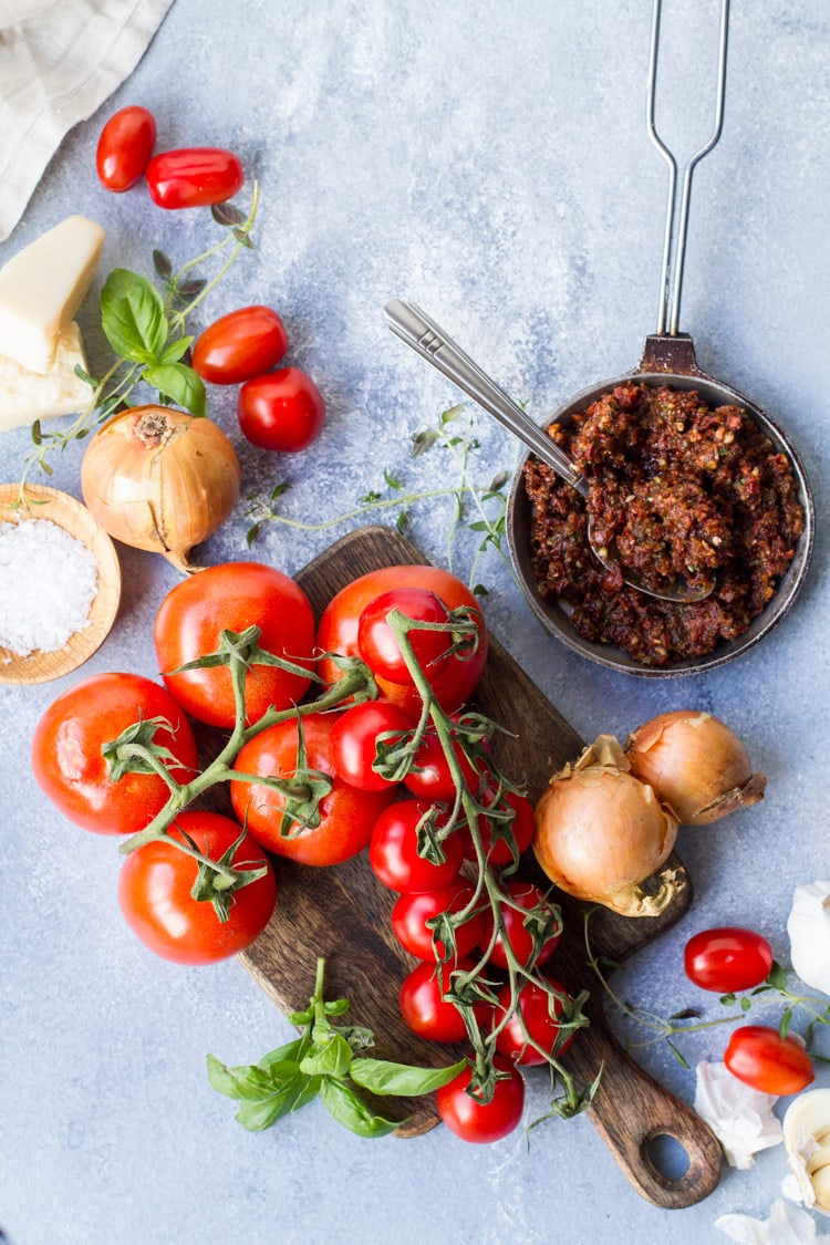 Ingredients to make roasted tomato soup; tomatoes on vines, basil, thyme, pesto etc.