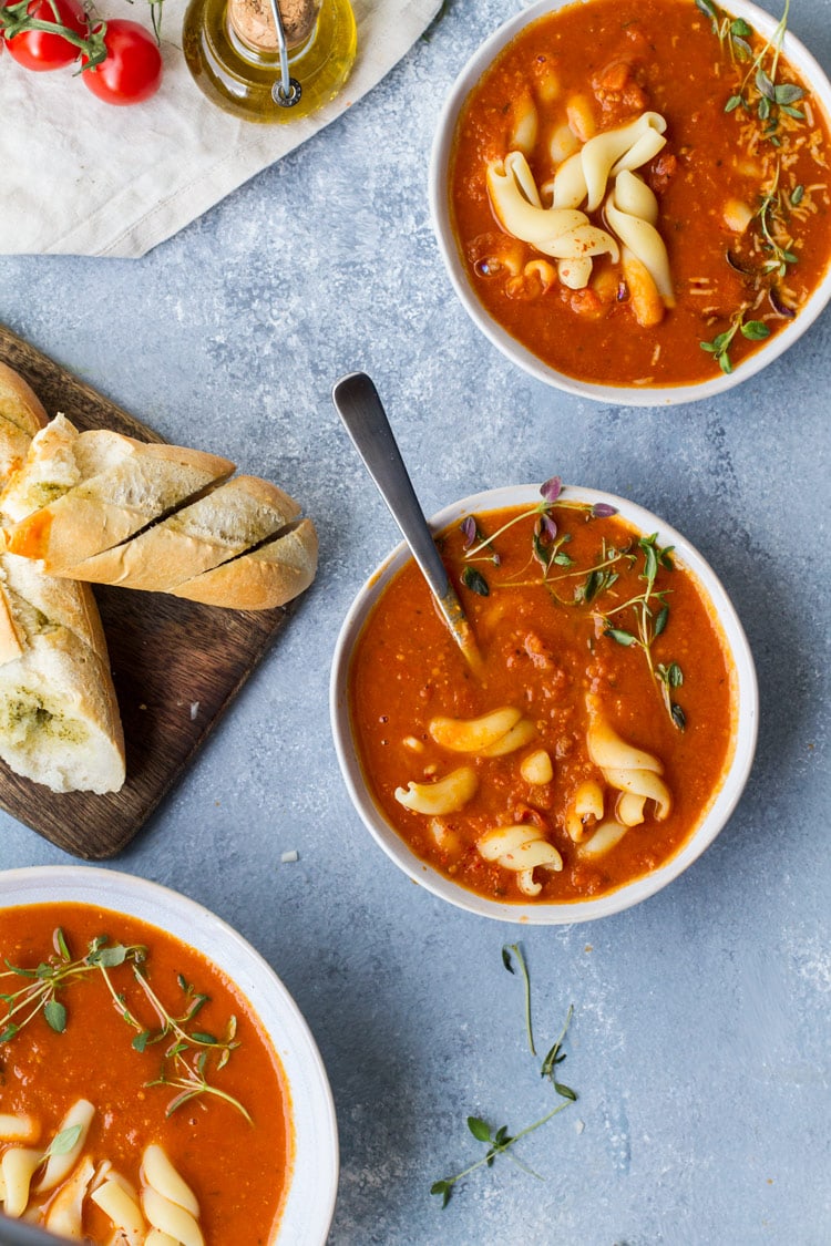 Three bowls of roasted tomato soup, garnished with pasta and fresh thyme.