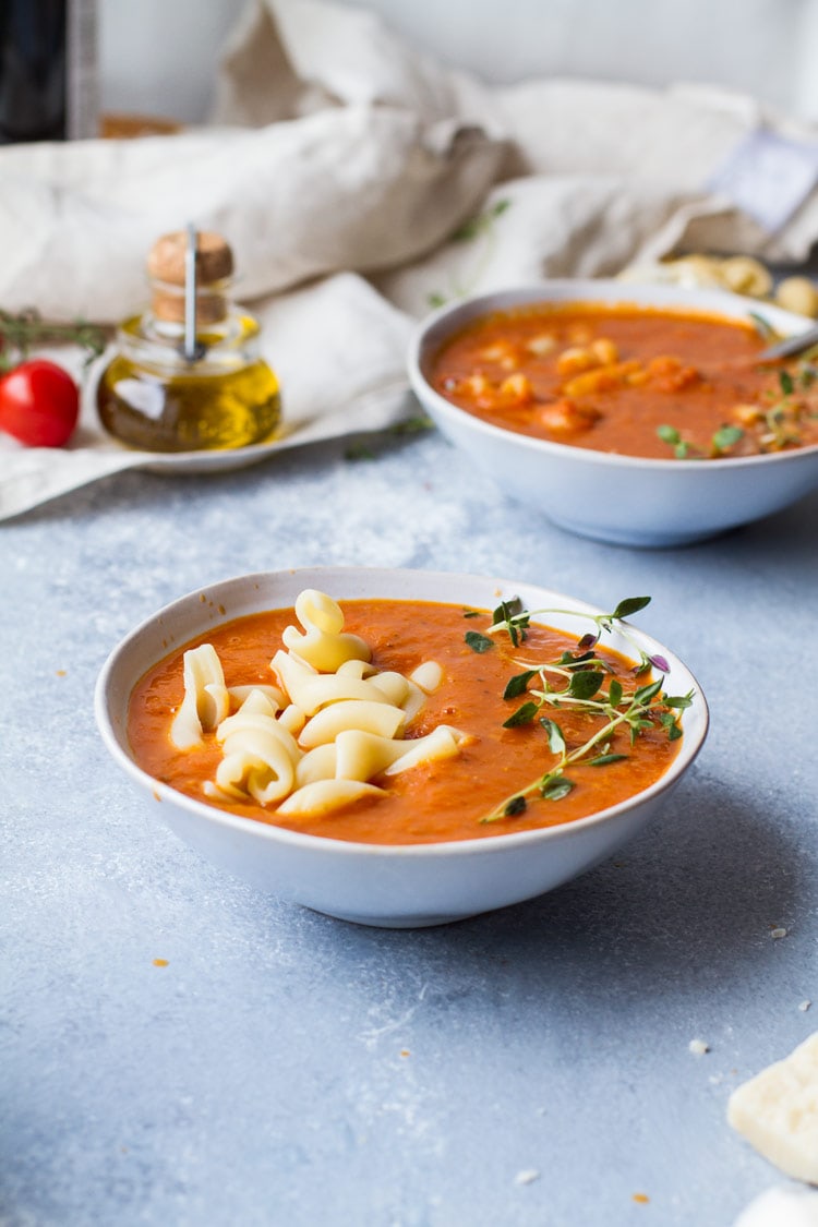Two bowls of roasted tomato soup, pasta and fresh thyme sprig.