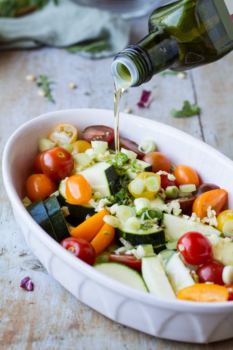 Pouring olive oil over vegetables for roasting.