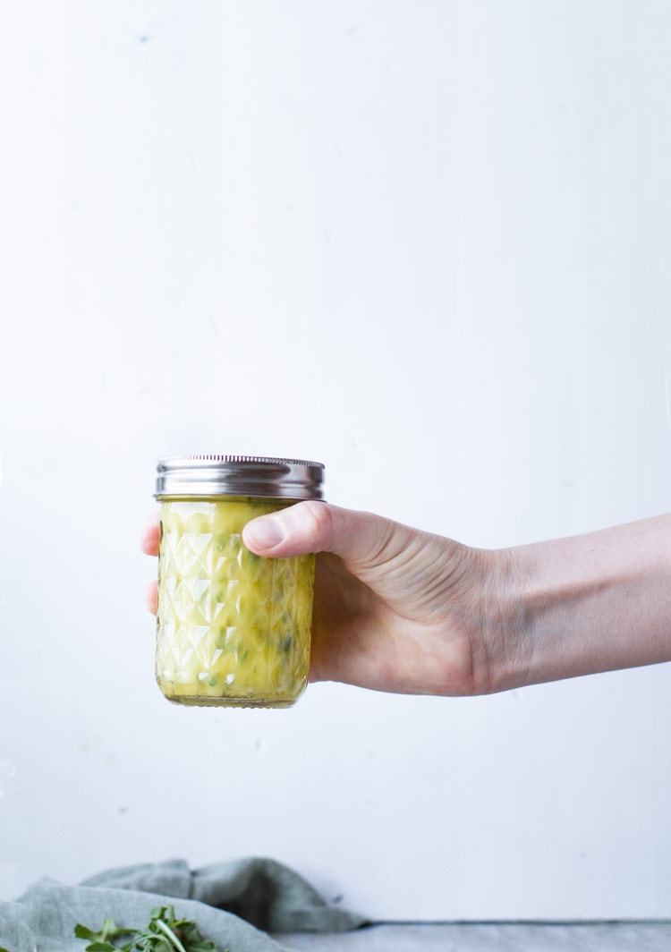 Hand holding a glass jar with a healthy pasta salad dressing.