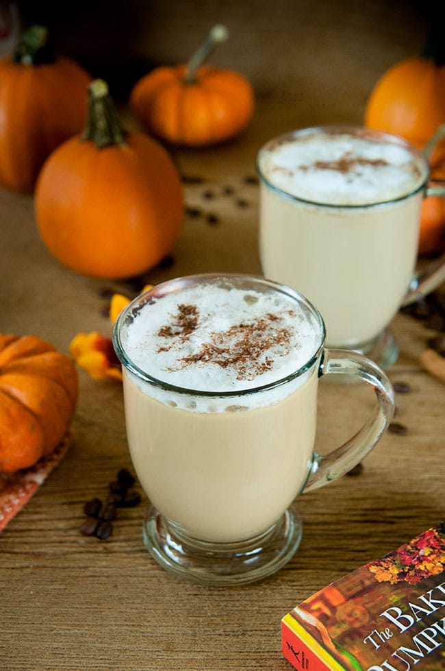 Spiked pumpkin spice latte in two clear mugs. Pumpkins as decoration in the background.
