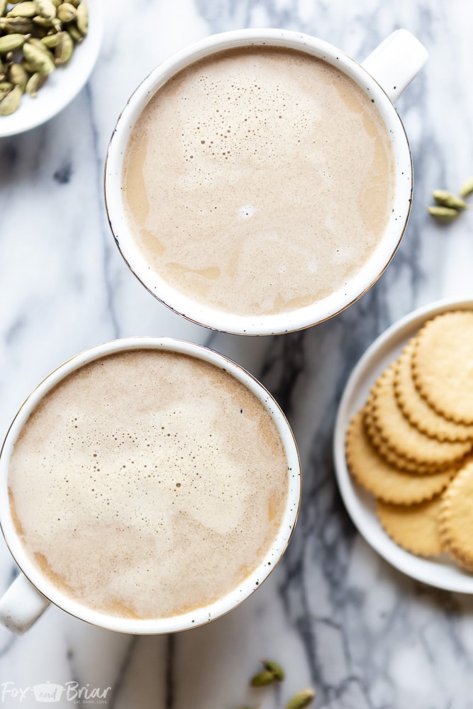 Cardamom latte in two cups, crackers on the table. Flatlay.