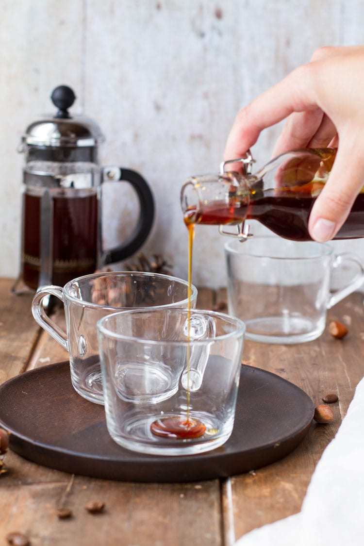 Pouring caramel sauce into clear glass cup.