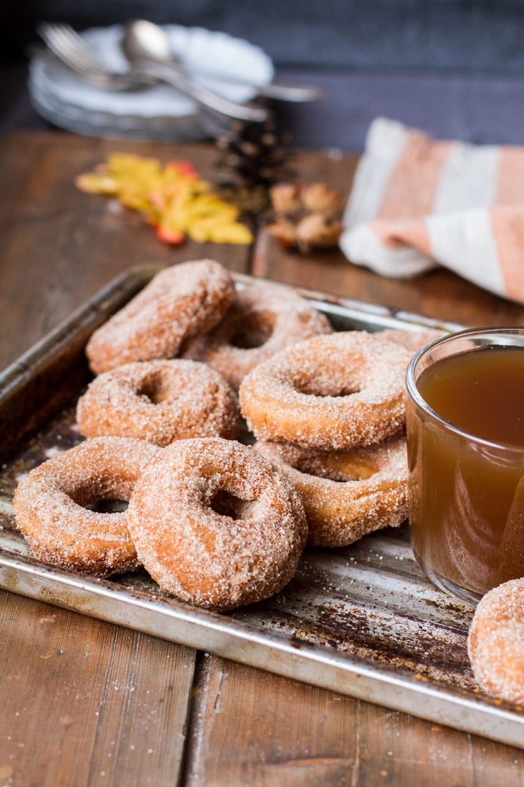 Donuts coated in cinnamon sugar and apple cider in a clear cup on a metal pan. 