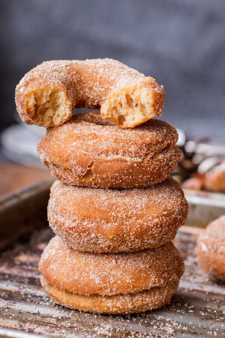 Three apple cider donuts stacked on top of each other and one half eaten on top.