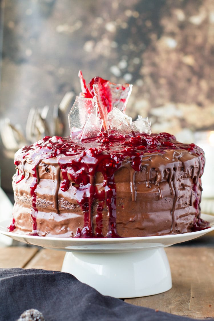 Cherry chocolate cake with sugar glass shards and cherry topping on a white cake stand.