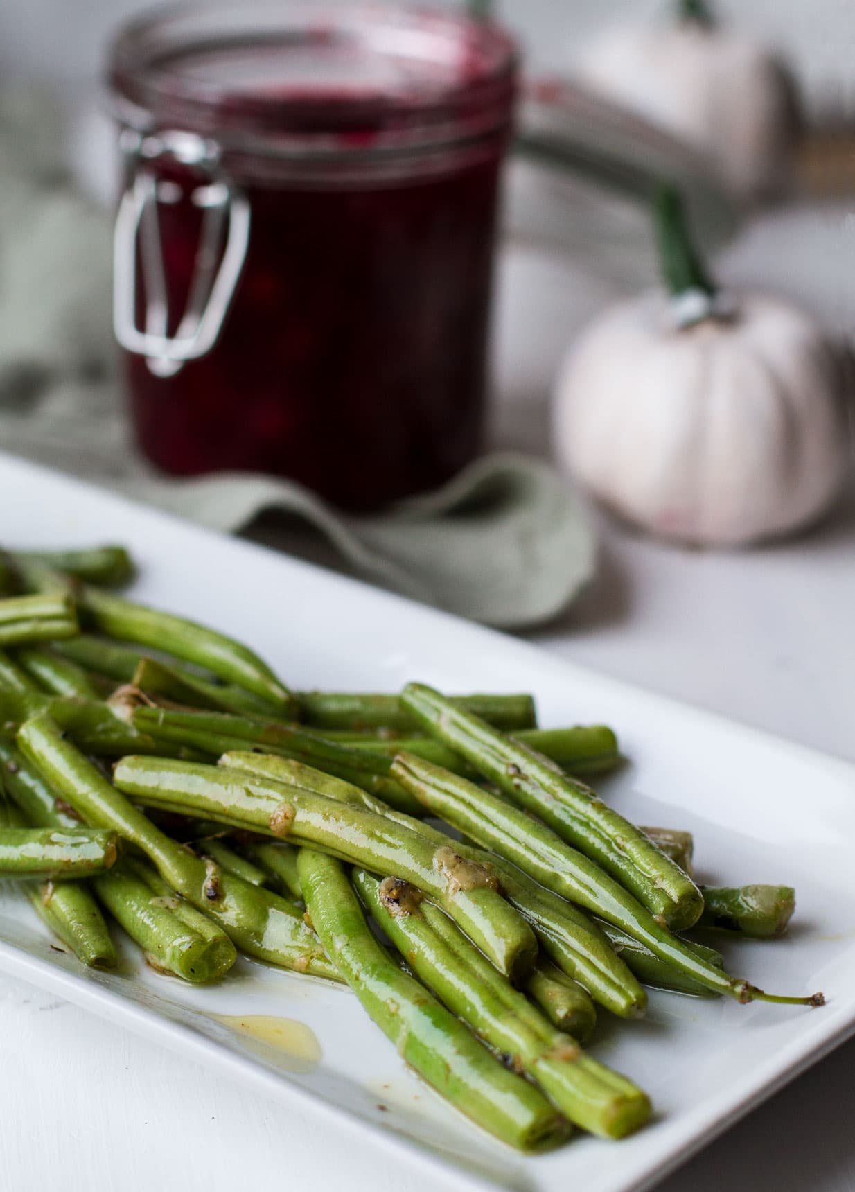 Garlic Parmesan Green Beans on a white, rectangular plate. Cranberry sauce in the background.