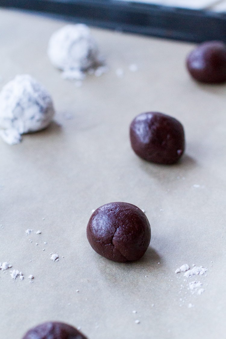 Balls of chocolate crinkle dough on parchment paper.