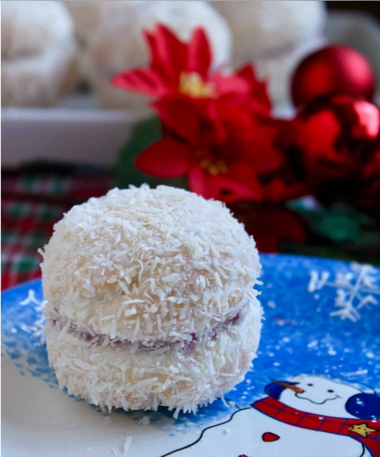 White cookies sandwiched with raspberry jam and coated in shredded coconut. On a blue snowman plate.