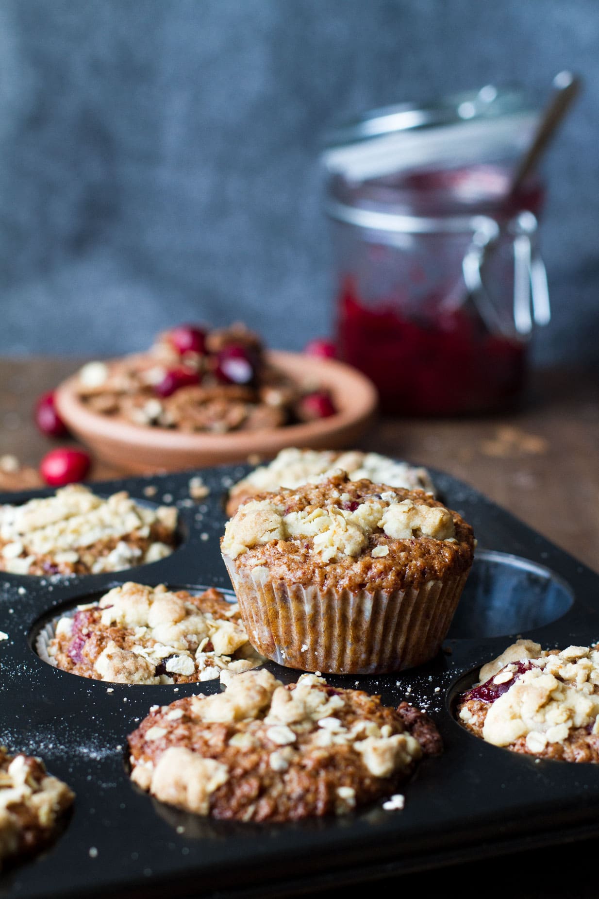 Cranberry sauce breakfast muffins on a muffin tin. Cranberry sauce in the background.