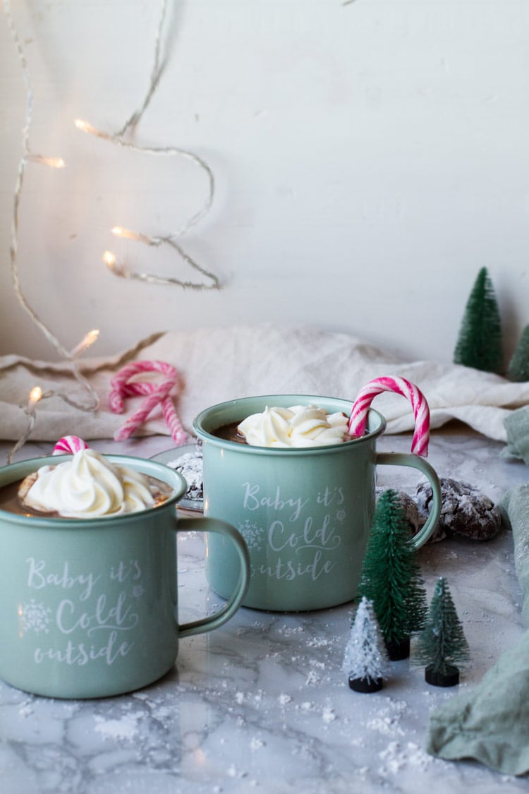 Two mint colored mugs with whipped cream and candy cane.