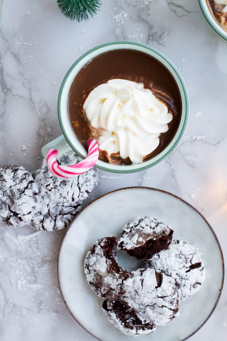 Mug with peppermint mocha, whipped cream and candy cane. Chocolate crinkle cookies on the side. Flatlay.