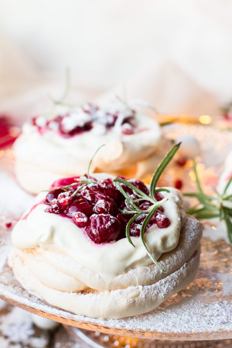 Christmas Pavlova Dessert with cherry sauce and rosemary sprig on a cake stand.