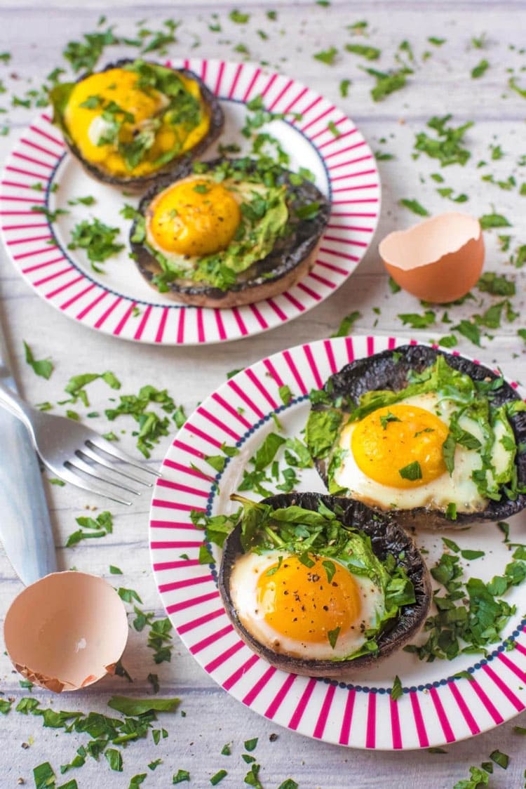 Two pink plates with two portobello mushrooms filled with baked eggs, each.
