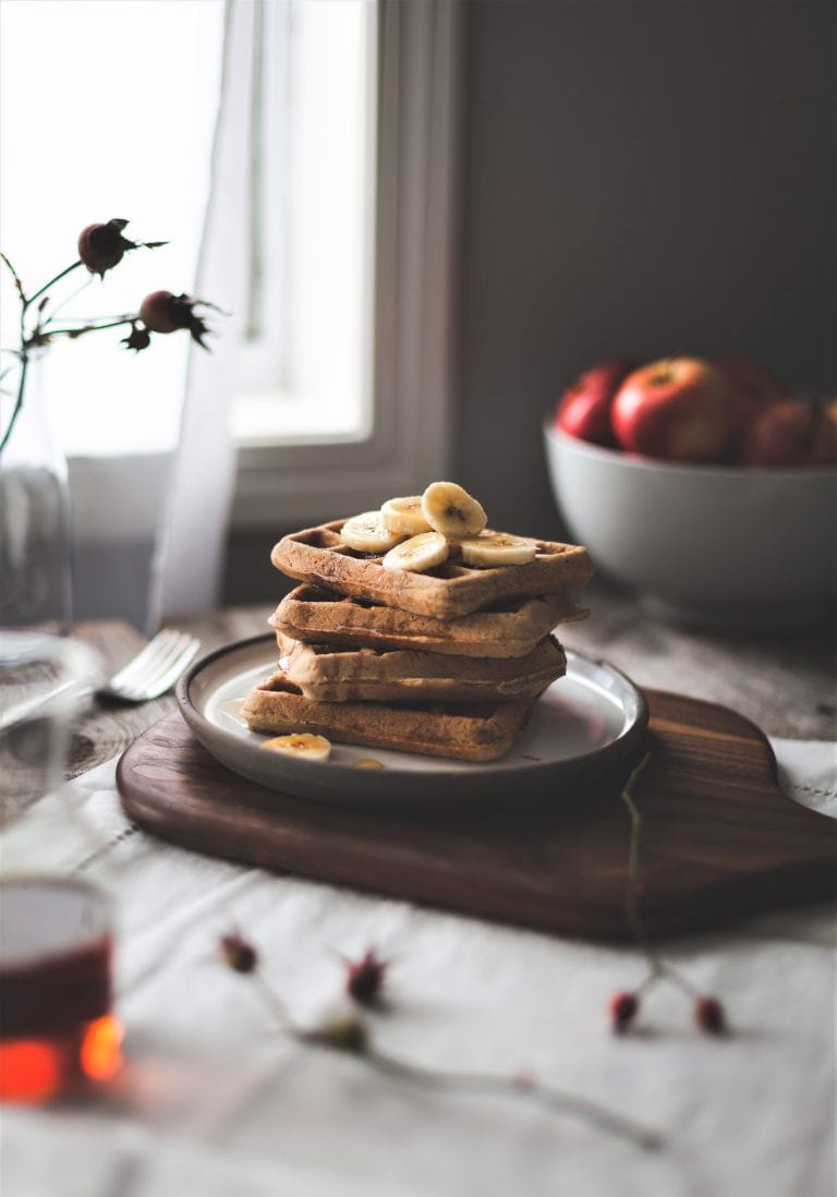 A stack of healthy breakfast waffles on a plate. Apples in the background.